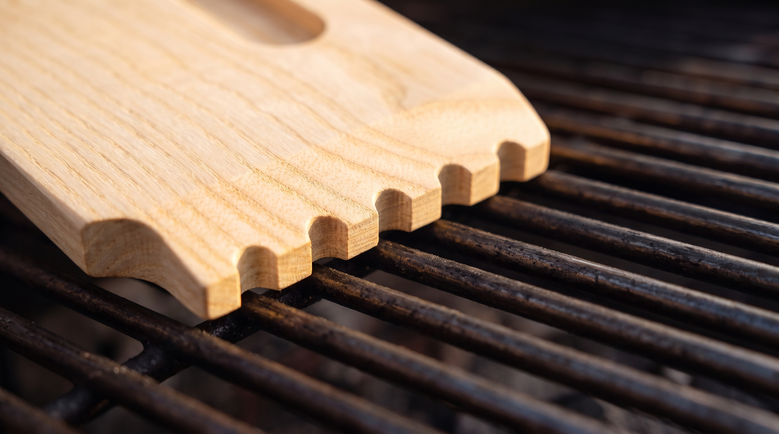 Brand new Skrapa wooden scraper with straight factory serrated edge resting on a grill grate
