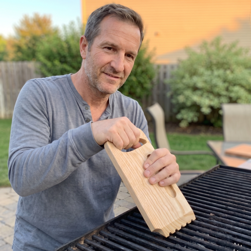 Dad using the Skrapa solid hardwood scraper on his backyard grill, grooves on the bars