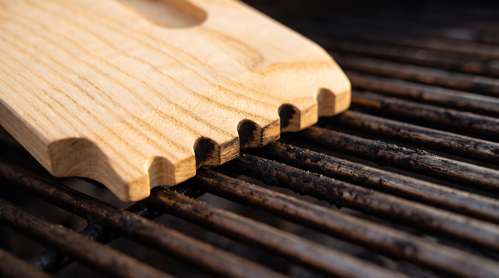Close-up of worn grooves in a wooden scraper edge matching grill grate bars